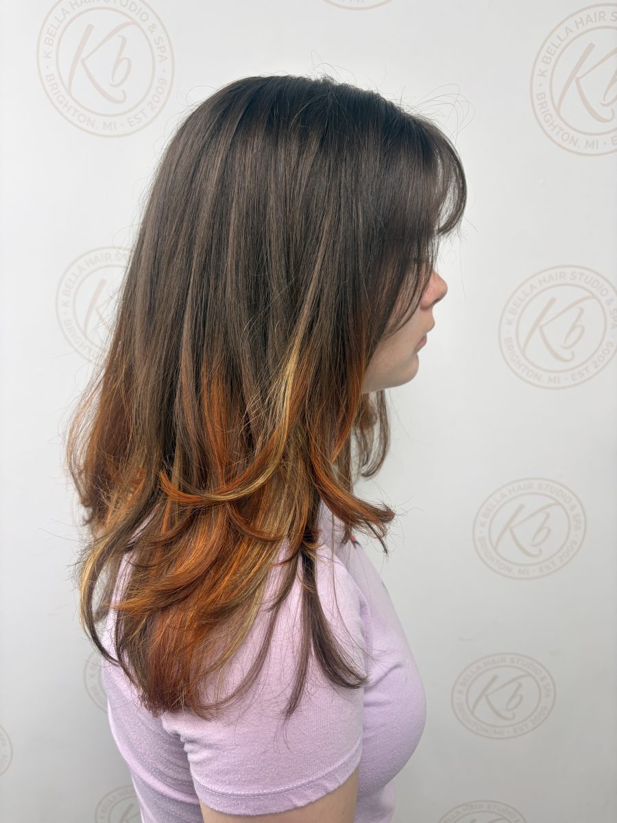 Side view of layered brunette hair with bright copper highlights in the layers, by Abbey French at K Bella Hair Studio & Spa in Brighton, MI