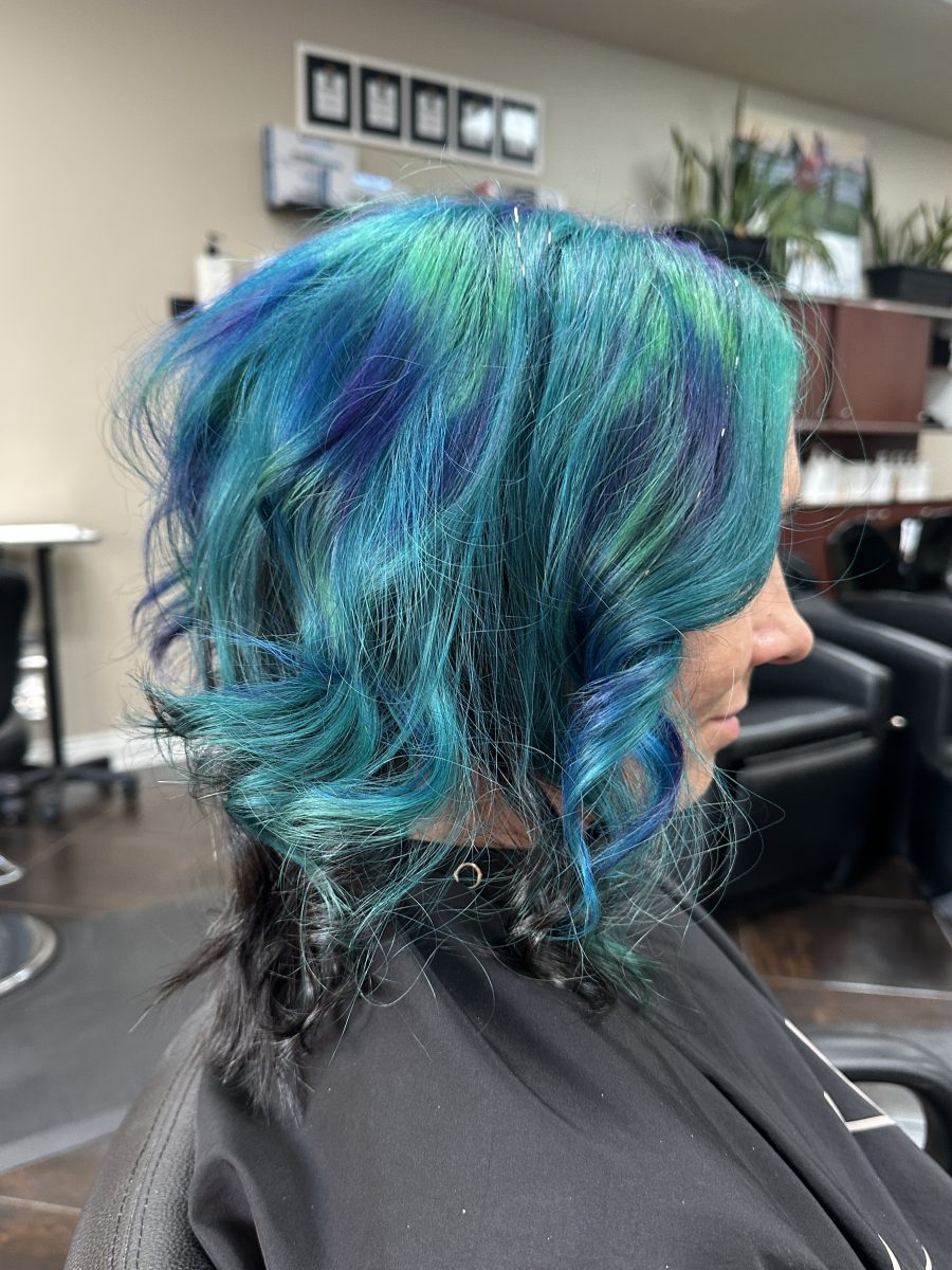Side view of shoulder-length hair with layered waves in blue and purple peacock tones by Liberty Greenwood at K Bella Hair Studio & Spa in Brighton, MI