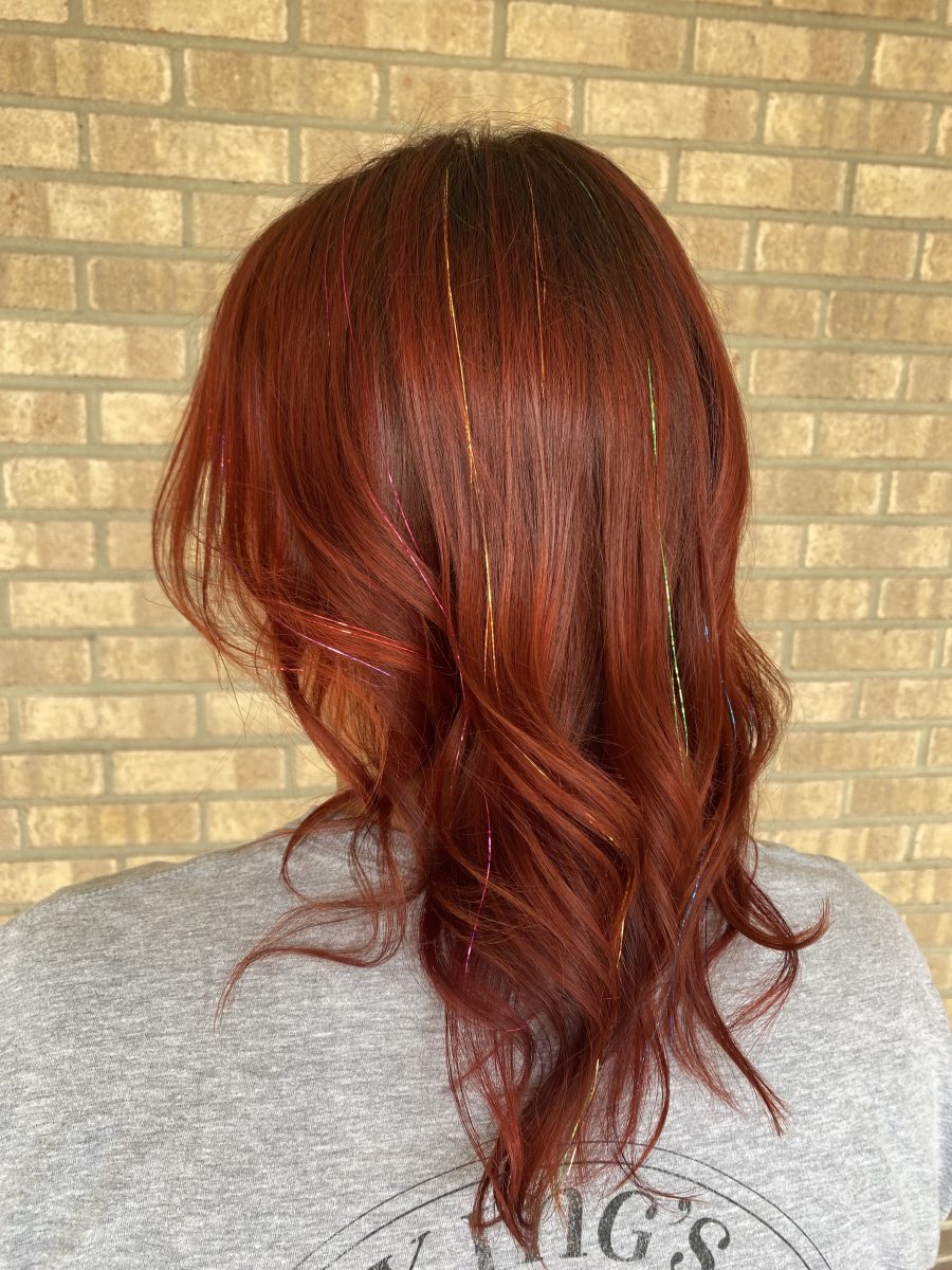 Back view of long wavy copper-toned hair with tinsel, shot against a brick wall by Allison Bowsher at K Bella Hair Studio & Spa in Brighton, MI