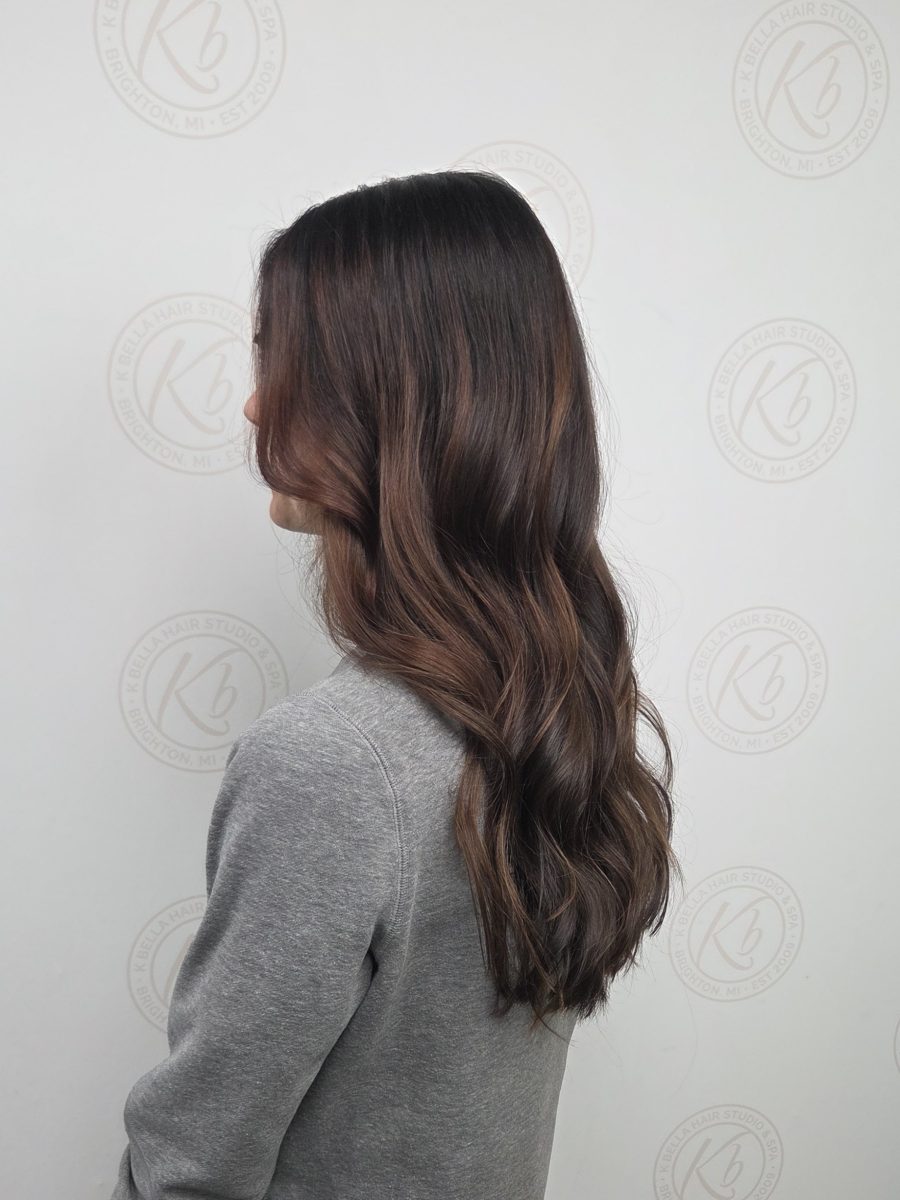 Three-quarter view of long wavy hair with warm mahogany color by Katie Rowe at K Bella Hair Studio & Spa in Brighton, MI