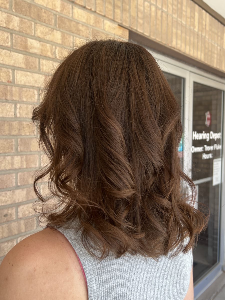 Back view of dark wavy hair with layered texture and warm-toned color in outdoor light by Kathryn McGinty at K Bella Hair Studio & Spa in Brighton, MI